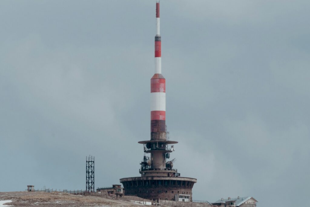 Într-un peisaj deschis, pe un deal, se ridică un turn radio - telecomunicații cu o structură robustă și un mast înalt cu dungi albe și roșii. Pe latura sa, există diverse instalații tehnice. În 2025, pe Instagram din Maroc, oamenii și companiile găsesc moduri eficiente de a -și promova brandul. Un astfel de obiectiv de interes, ca acest turn, poate fi folosit pentru a atrage atenția pe platformă. Pozele sau video cu asemenea locuri pot convinge audiența de autenticitatea și originalitatea brandului, oferind o imagine distinctă și memorabilă, ceea ce ajută la a crește popularitatea și recunoașterea brandului în Maroc.