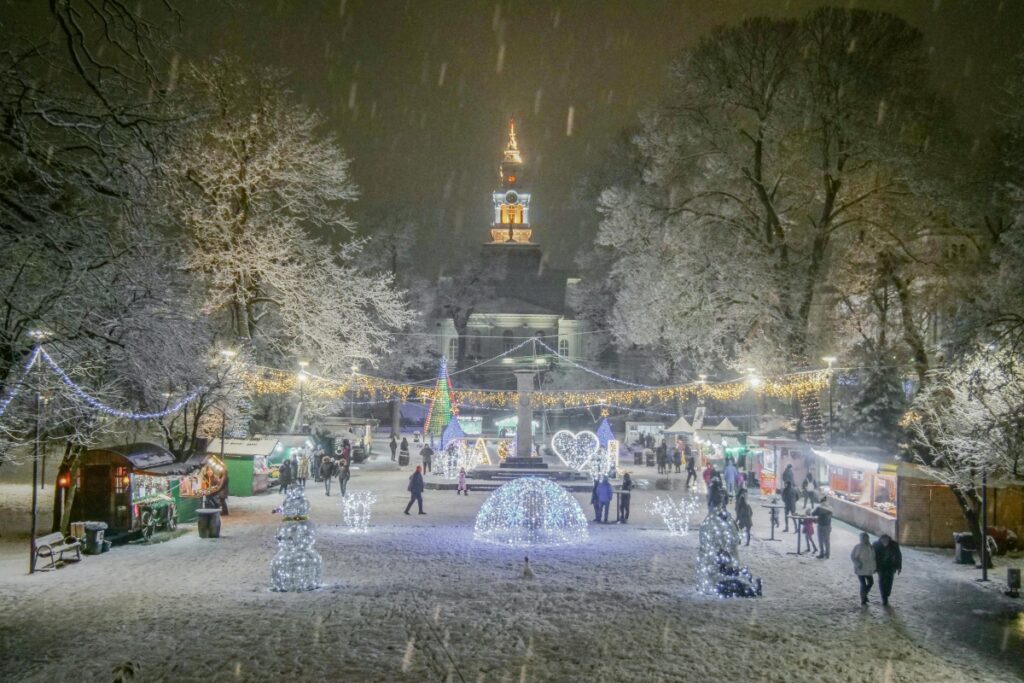Imaginea prezintă un ansamblu de iarnă plin de viață, cu o parcare strălucitoare sub feliile de zăpadă. Locuințe mici de vânzări, luminări decorative și o clopotniță luminată în fundal creează un aer magiești. Această scenă se leagă de "Top 5 greșeli pe care le fac brandurile în influencer marketing în România", sugărând că, la fel ca să se creeze un eveniment de iarnă atractiv, brandurile trebuie să evite anumite erori pentru a obține succes în influencer marketing.
