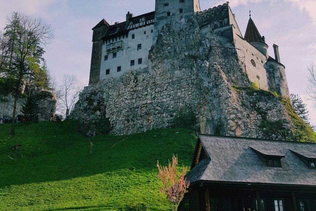 Imaginea prezintă Castelul Bran, un monument iconic ridicat pe o deală, cu ziduri de piatră robuste și o arhitectură medievală. Pe lângă el, se află o casă cu acoperiș din scânduri de lemn. Padurea și pelușul verde de iarnă completează peisajul. Pe YouTube, există numeroase canale marocane care câștigă popularitate. Un astfel de loc iconic ca Castelul Bran ar putea fi subiectul videoclipurilor pe aceste canale, atragând atenția asupra patrimoniului românesc și a istoriei sale legendar. Marocanezii care urmăresc aceste canale pot descoperi noi aspecte ale diferitelor locuri de interes din Europa, cum ar fi acest Castel, și astfel se poate dezvolta o comunitate de entuziasti pentru turism și istorie pe platforma video.